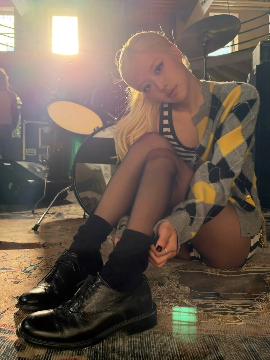 아가일 가디건을 입은 여성이 드럼 세트 앞에서 앉아 있음