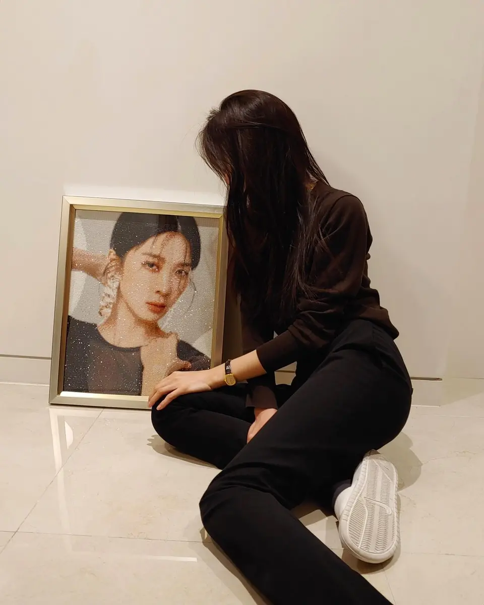 한 여성이 바닥에 앉아 액자에 담긴 자신의 사진을 바라보고 있다.