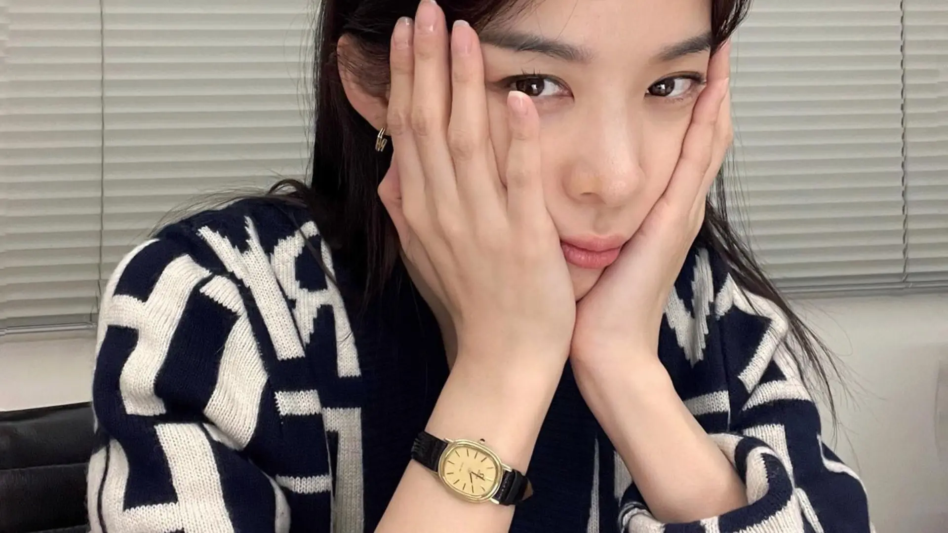 한 여성이 손으로 턱을 괴고 카메라를 응시하고 있다.