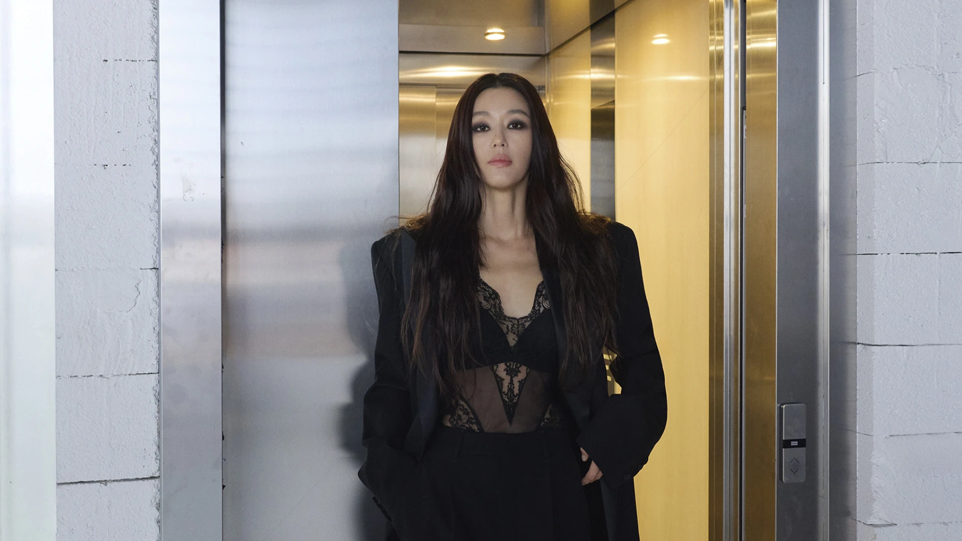 전지현이 검은색 정장을 입고 엘리베이터 앞에서 서 있다.